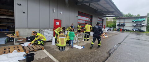 Feuerwehrleute in gelben Jacken arbeiten gemeinsam vor einer Lagerhalle, um Ausrüstungen zu ordnen und vorzubereiten.
