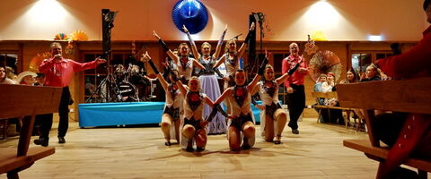 Eine Tanzgruppe führt eine lebhafte Choreografie bei einer Feier in einem festlich dekorierten Saal auf.
