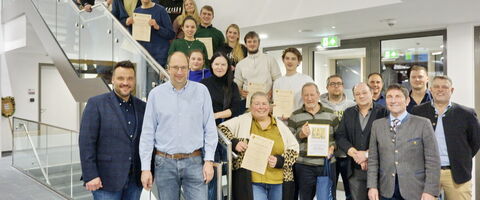 Eine Gruppe von Menschen posiert auf einer Treppe mit Urkunden während der FFW-Jahreshauptversammlung 2026.