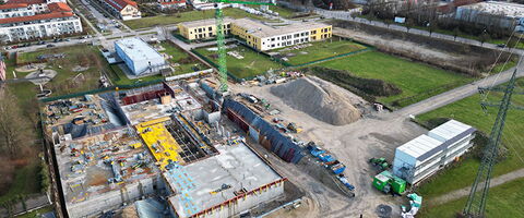 Eine große Baustelle mit einem Kran und mehreren Gebäuden in einer urbanen Umgebung entwickelt sich weiter.