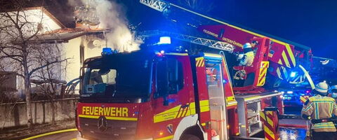 Ein Feuerwehrauto der Freiwilligen Feuerwehr Unterföhring löscht nachts einen brennenden Dachstuhl.