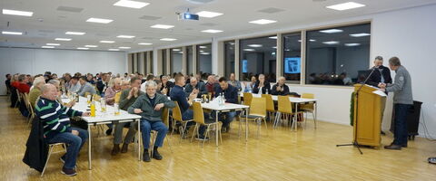 Menschen versammeln sich in einem großen Saal zur Feuerwehr-Jahreshauptversammlung 2026, während ein Vortrag gehalten wird.